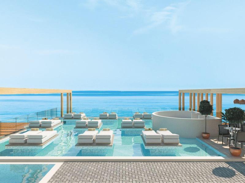 Luxusní střešní bazén s lehátky, kabinami a výhledem na oceán pod jasnou oblohou.