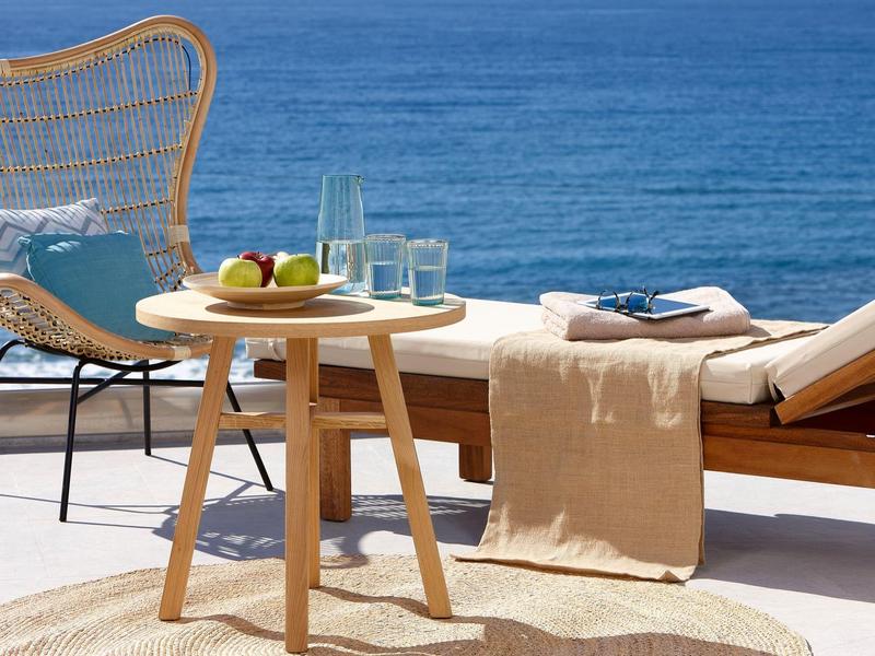 Venkovní posezení se dřevěným stolkem, židlí a lehátkem u modrého moře.
