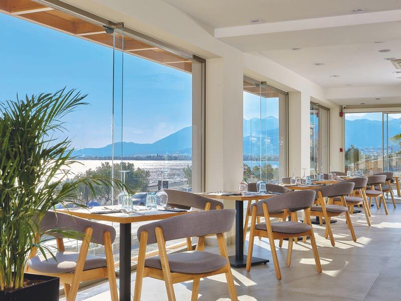 Světle hotelová restaurace s průhlednými skleněnými stěnami a stoly s výhledem na oceán.