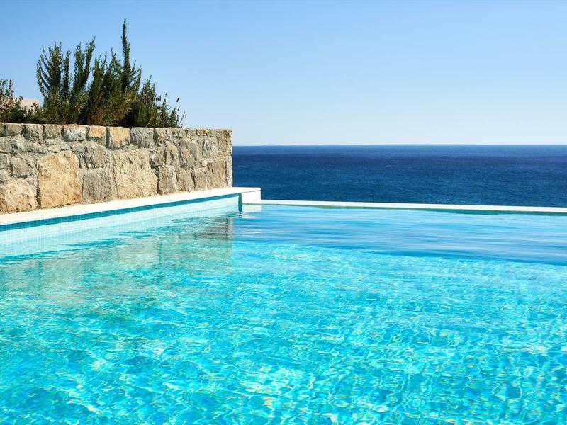 Čirý infinity bazén s výhledem na klidné modré moře pod jasnou oblohou.