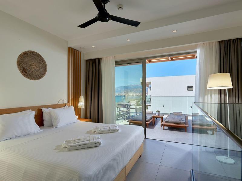 Moderní hotelový pokoj s velkou postelí, stropním ventilátorem, skleněným balkonem a venkovním posezením.