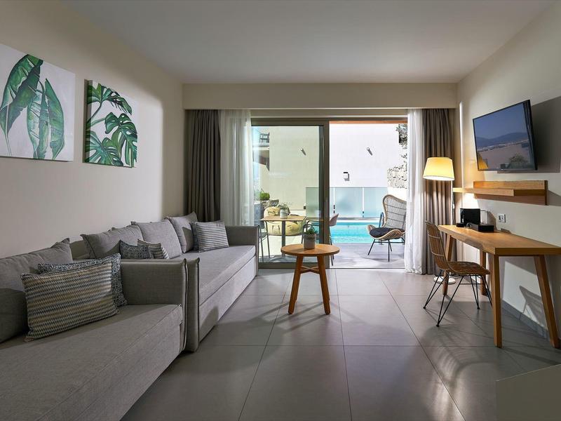 Moderní hotelový pokoj s pohovkami, uměním, TV, stolem a balkonem s výhledem na bazén.