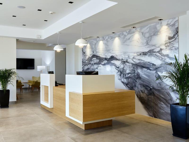 Moderní hotelová recepce s dřevěnou přepážkou, mramorovou stěnou a květinami v květináčích.