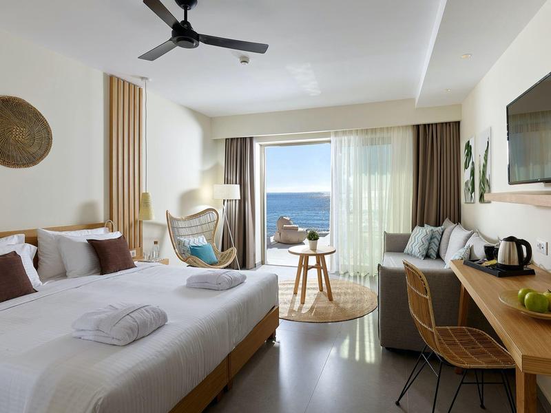 Moderní hotelový pokoj s velkou postelí, posezením, psacím stolem a balkonem s výhledem na oceán.