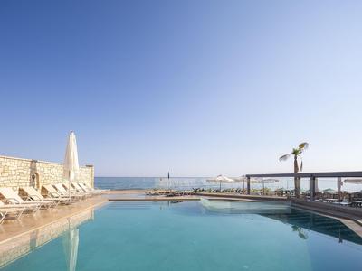 Piscina con tumbonas y vista al mar bajo un cielo azul claro.