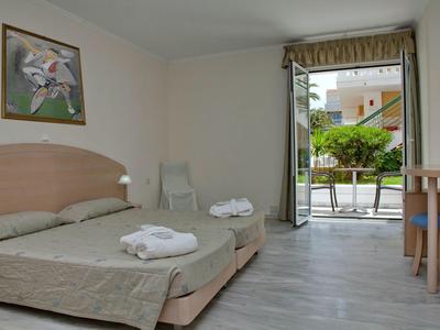 Habitación de hotel con dos camas individuales, puerta del balcón abierta y vista a la terraza y jardín