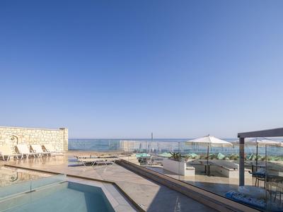Terraza con piscina, sombrillas y vista al mar bajo un cielo despejado.