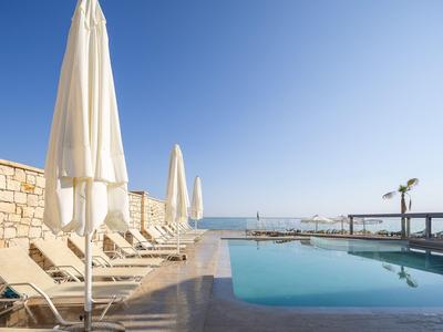 Piscina con tumbonas y sombrillas junto al mar bajo un cielo despejado.