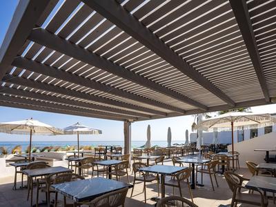 Terraza soleada del hotel con mesas, sillas y grandes sombrillas bajo una pérgola de madera.