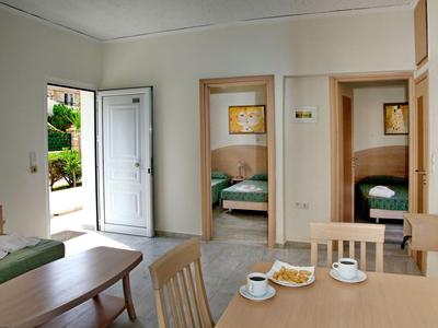 Habitación de hotel luminosa con puerta abierta, mesa de comedor, dos dormitorios y servicio de café.