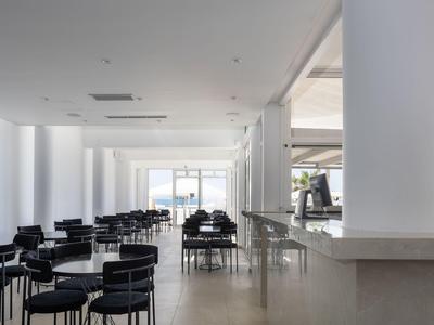 Área de comedor moderna vacía con sillas negras y grandes ventanas con vista al mar.