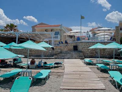 Playa con tumbonas y sombrillas frente a un edificio bajo un cielo azul con nubes.