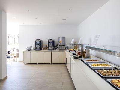 Área de buffet con varias opciones de desayuno en una habitación moderna y luminosa.