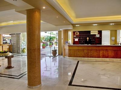 Vestíbulo de hotel con recepción, suelo de mármol y columnas en una habitación luminosa.