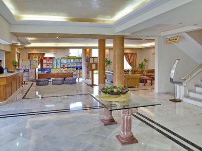 Área luminosa del vestíbulo del hotel con recepción, mesa de vidrio y suelo de mármol.