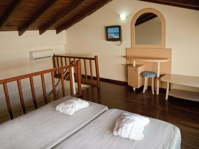 Habitación acogedora con dos camas individuales, batas y muebles de madera bajo un techo inclinado.