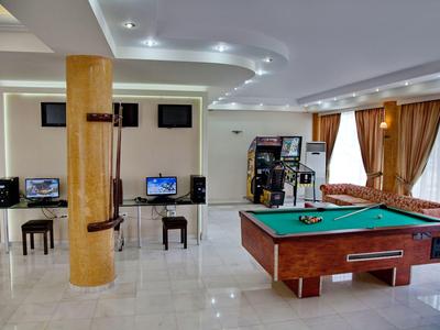 Sala de recreo con mesa de billar, máquinas arcade y zona de asientos con cortinas en las ventanas.