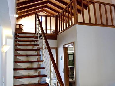 Interior moderno con escalera de madera, techo alto y barandilla de madera en una habitación luminosa.