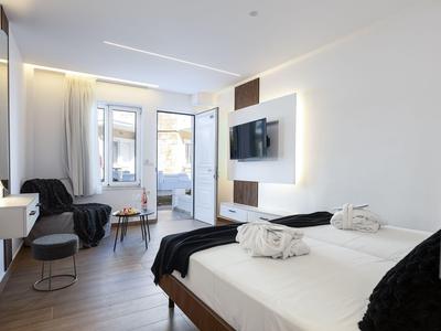 Habitación de hotel moderna con dos camas individuales, televisión y área de estar junto a la ventana.