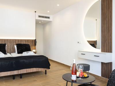 Habitación de hotel moderna con cama doble, suelo de madera y pequeña mesa con bebidas y fruta.
