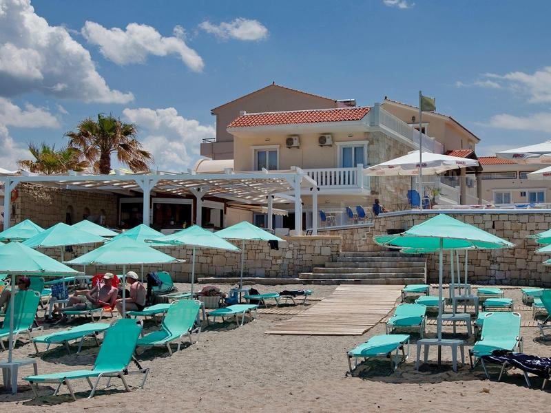 Plaża z turkusowymi leżakami i parasolami przed budynkiem hotelu.