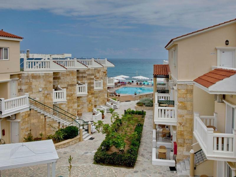 Widok na kompleks hotelowy z balkonami i morzem w tle pod niebieskim niebem.