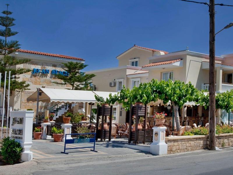 Zewnętrze hotelu z zielonymi roślinami, stołami, parasolami i cichą ulicą.