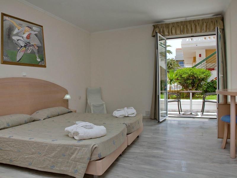 Prosty pokój hotelowy z dwoma pojedynczymi łóżkami i balkonem z widokiem na zieleń.