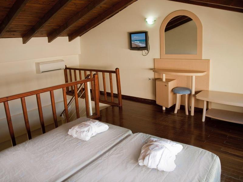 Prosty pokój hotelowy z dwoma łóżkami, szlafrokami, drewnianą podłogą i toaletką pod skośnym sufitem.