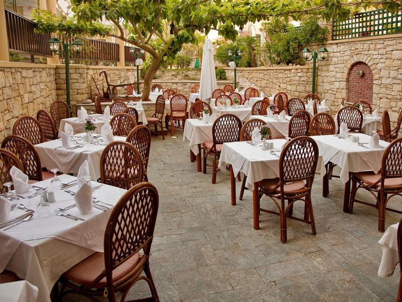 Restauracja na świeżym powietrzu z nakrytymi stołami i krzesłami na kamiennej podłodze pod drzewami.