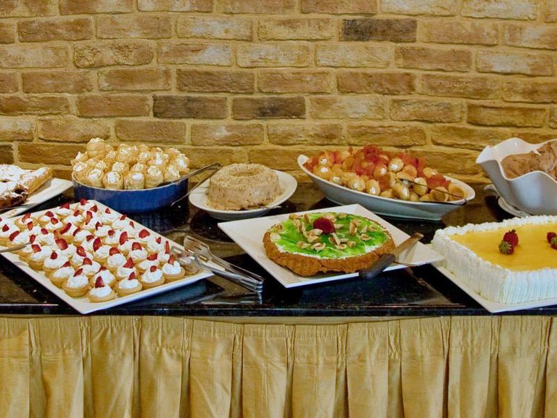 Bufet z różnymi gorącymi i zimnymi potrawami na stole na tle ceglanej ściany.