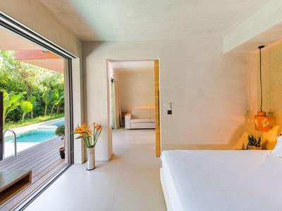 Chambre d'hôtel moderne avec grand lit, vue sur jardin et piscine par porte coulissante ouverte