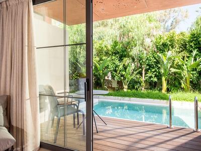 Terrasse avec piscine et verdure luxuriante, vue à travers une grande porte vitrée depuis l'intérieur