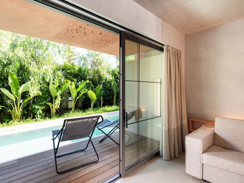 Vue d'une chambre sur une terrasse avec deux chaises et une piscine, entourée de plantes vertes.