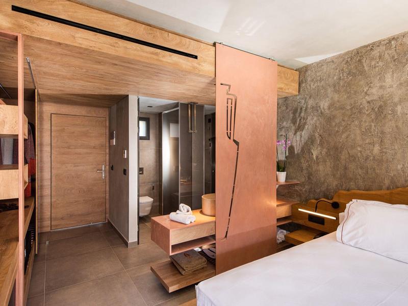 Chambre d'hôtel moderne avec détails en bois, lit double, salle de bain ouverte et tons chauds.