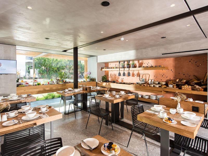 Restaurant d'hôtel moderne avec tables en bois, chaises noires et un buffet le long du mur.