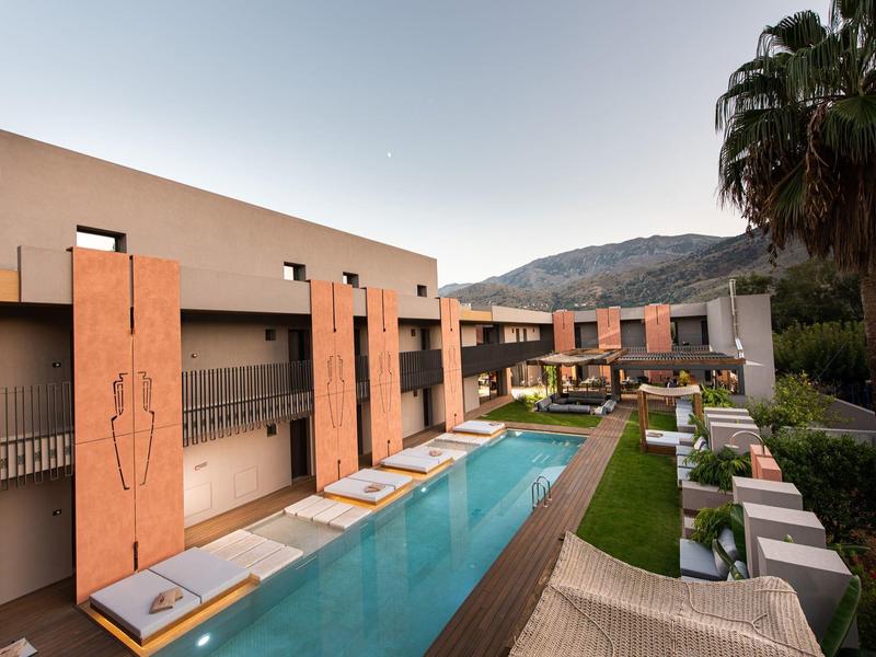 Hôtel moderne avec piscine extérieure, transats et palmiers dans un cadre montagneux