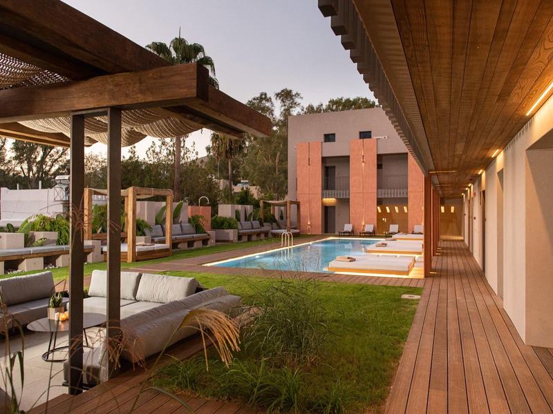 Espace hôtelier moderne avec piscine, terrasses en bois et fauteuils d'extérieur confortables au crépuscule.