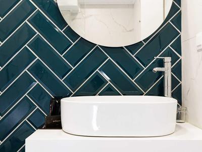 Moderne badkamer met ronde spiegel, witte wastafel en donker groene wandtegels.