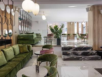 Modern lobby area with green sofas, round tables, and decorative mirrors on the wall.
