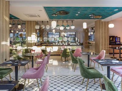 Modern hotel lounge area with colorful chairs, lamps, and decorative ceiling artwork.