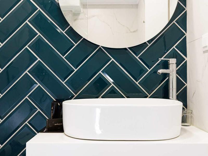 Moderne badkamer met ronde spiegel, witte wastafel en donker groene wandtegels.