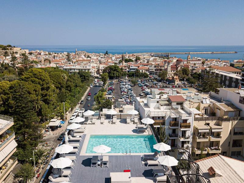 Uitzicht op een stad met haven, met een zwembad en witte parasols op de voorgrond.