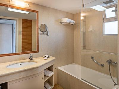 Modern bathroom with bathtub, wall mirror, beige tiles, and towel shelf.