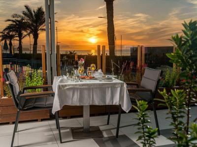 Tavolo da pranzo all'aperto con sedie e vista al tramonto tra palme e piante.
