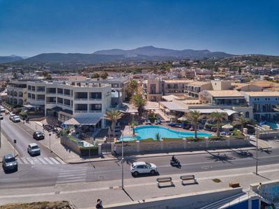 Hotel with outdoor pool near a busy road, surrounded by buildings and distant hills.
