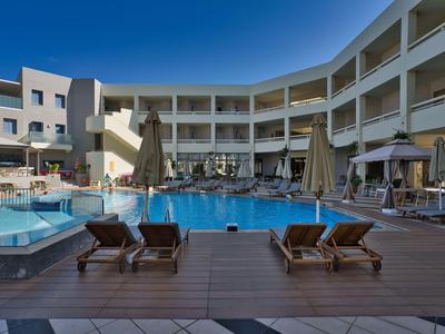 Hotel met zwembad en ligstoelen op een houten terras bij heldere lucht.