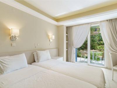 Bright hotel room with twin beds, wall sconces, and sliding glass doors to a balcony.