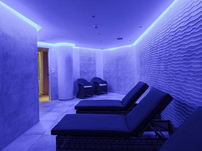 Relaxing spa room with lounge chairs and textured walls lit by blue LED lights.