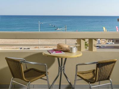 Balcon avec table et deux chaises donnant sur la plage et la mer sous un ciel clair.